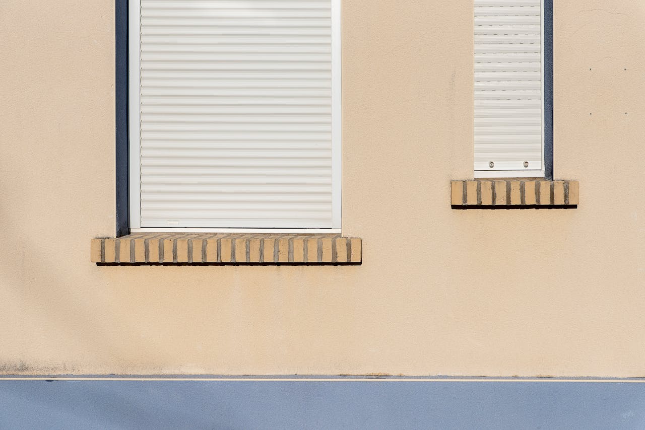 A beige building facade with closed white roller blinds and minimal architectural design.